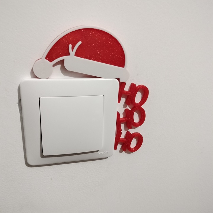 Decoratiune de Craciun inedita pentru intrerupator sau priza, avand sloganul Ho Ho Ho si Caciula lui Mos Craciun, culori rosu glitter si alb, aspect unic, 125x105x5 mm